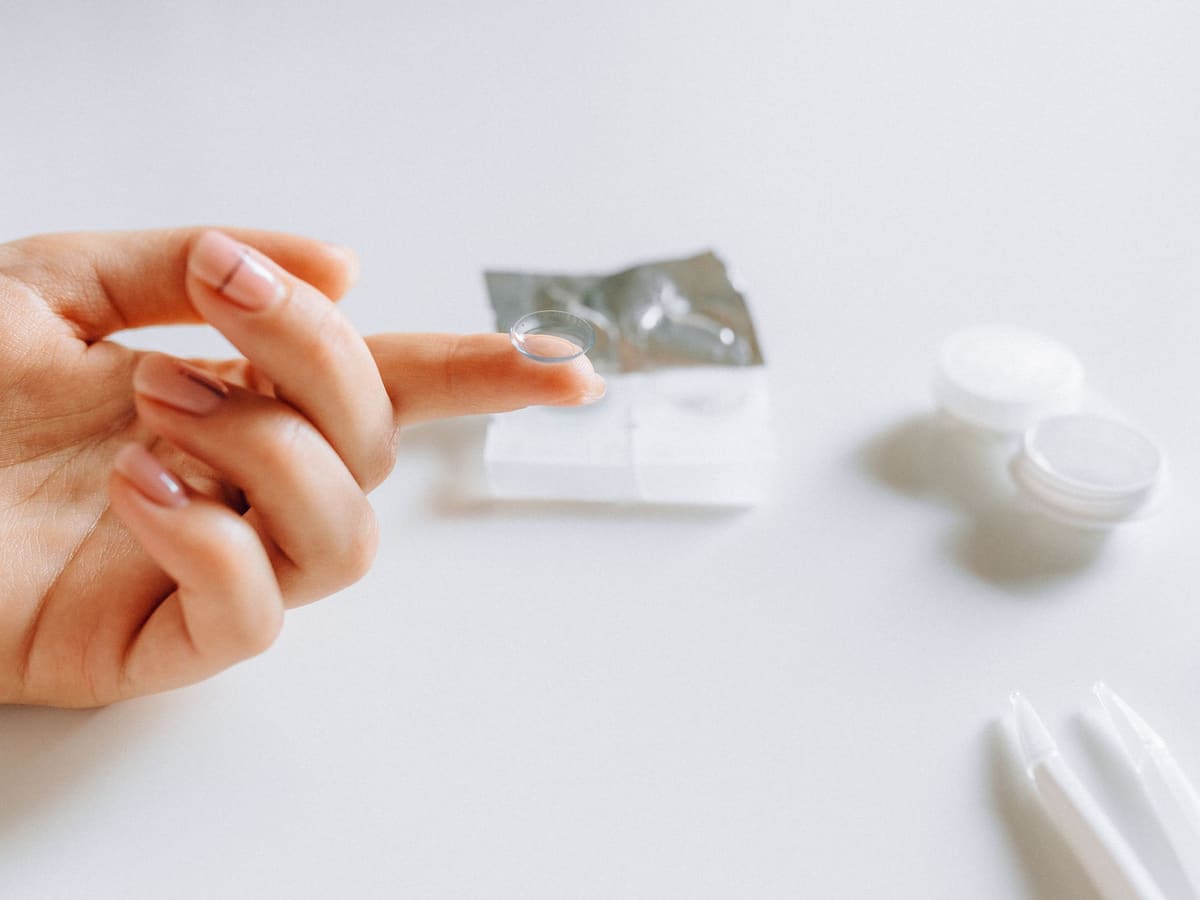 A soft contact lens balanced on a fingertip beside a lens case