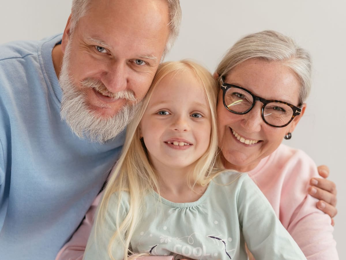 Smiling grandparents with their young granddaughter; the grandmother wears glasses